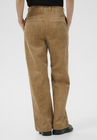Bruine corduroy, wijde broek met een gestructureerd oppervlak, zijzakken en achterzakken met paspel. Afgewerkt met een klassieke tailleband en riemlussen.