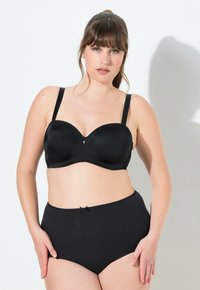Zwarte beugel bh van glad, satijnachtig materiaal met verstelbare bandjes. Gecombineerd met hoge zwarte slips met een strikaccent.