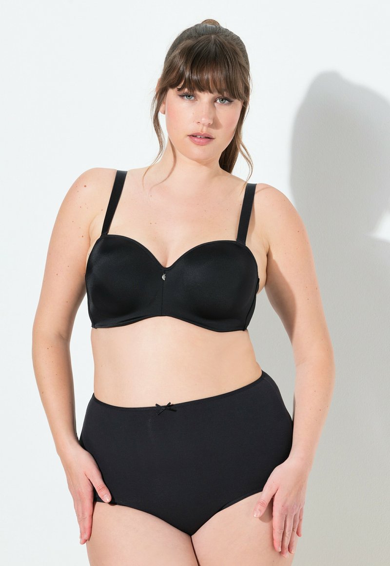 Zwarte beugel bh van glad, satijnachtig materiaal met verstelbare bandjes. Gecombineerd met hoge zwarte slips met een strikaccent.