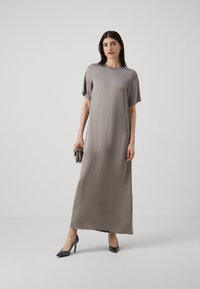 Rochie maxi din satin moale, gri deschis, cu manșete scurte, decolteu rotund, textură netedă, completată de pantofi cu toc înalt negri și o poșetă metalică.