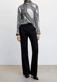 Haut à manches longues noir et blanc avec des motifs de lignes ondulées, associé à un pantalon noir taille haute et des escarpins noirs pointus.