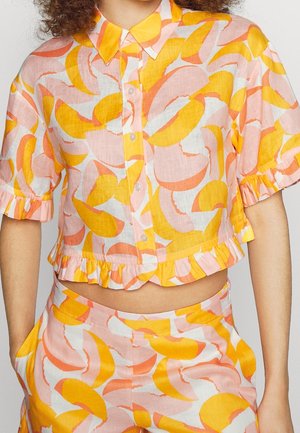 Conjunto de camisa corta y pantalones con formas abstractas en naranja, amarillo y rosa, que presenta botones delanteros, mangas cortas con volantes y dobladillo con volantes.
