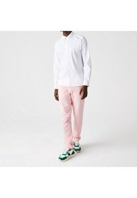 Camisa blanca de botones de manga larga, pantalones rosas y zapatillas verde y blancas. El conjunto presenta un corte clásico con una textura suave.