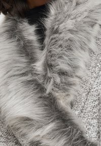 Tejido gris texturizado con un suave cuello de piel sintética. El cuello presenta diferentes tonos de gris, creando una apariencia mullida.