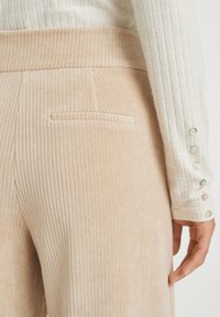 Béžové kordové kalhoty s vertikálním žebrováním, se boční kapsou. Doplněné strukturovanou bílou košilí s dlouhým rukávem a knoflíkovými detaily.