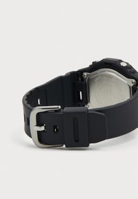 Curea de ceas din silicon negru cu o cataramă metalică argintie. Prezintă o suprafață texturată și un cadran de ceas rectangular cu un spate din oțel inoxidabil.
