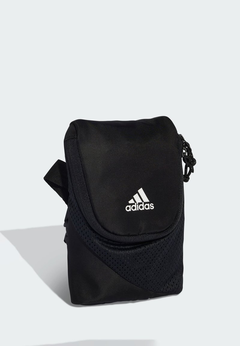 Zwarte kleine Adidas schoudertas met klep en wit Adidas-logo aan de voorkant, afgebeeld tegen een lichtgrijze achtergrond.