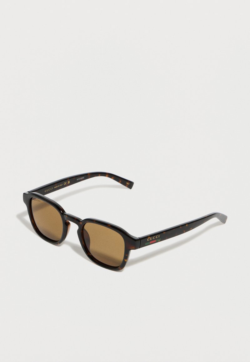 Lunettes de soleil rectangulaires en écaille de tortue avec des verres marron, arborant le logo Gucci et une bande verte-rouge-verte sur les branches.