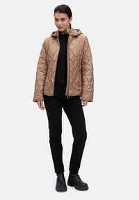 Beżowa pikowana kurtka z kapturem, z zamkiem błyskawicznym z przodu i bocznymi kieszeniami. Czarne spodnie i masywne czarne botki dopełniają zestaw.