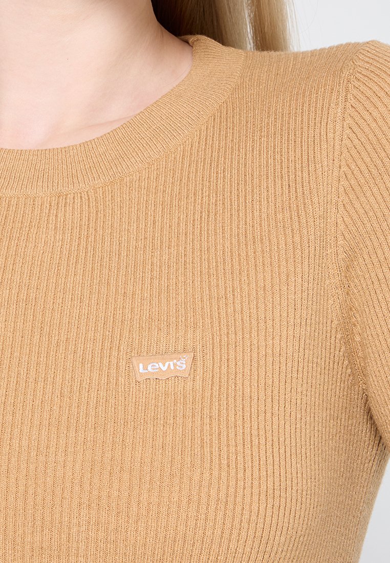 Beige gerippter Strickoberteil mit rundem Ausschnitt; verfügt über ein helles Levi's-Logoschild auf der Brust. Glatte Textur, taillierte Passform.