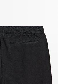 Zwarte corduroy broek met een gestructureerd oppervlak, voorzien van een elastische tailleband en een enkele achterzak.