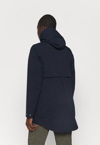 Marineblaue wasserdichte Jacke mit Kapuze, ausgestattet mit einem Rückeneinsatz, einem längeren hinteren Saum und Druckknopf-Manschetten. Glatte Textur, minimalistisches Design.