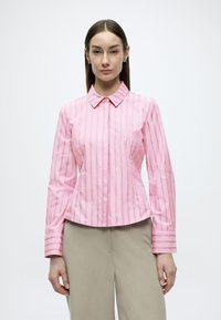 Ροζ πουκάμισο με κάθετες λευκές ρίγες, μυτερό γιακά και μακριά μανίκια με ριγέ μανσέτες. Ραμμένο εφαρμοστό.