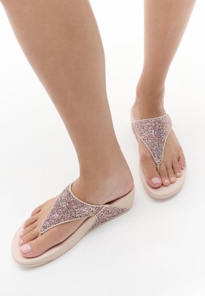 Piedi con sandali zeppa rosa con cinturini glitterati su sfondo bianco, con unghie dei piedi dipinte.