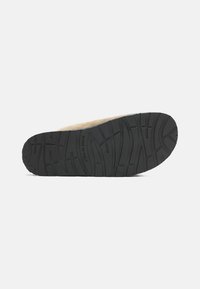 Zwarte rubberen zool met getextuurde loopvlakpatronen en beige suède bovenkant. De onderkant toont de indruk "MADE IN ITALY".