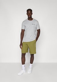 Grå t-shirt med korte ærmer og sort logo, parret med olivengrønne shorts med en lynlås-lomme. Båret med hvide sneakers og sokker.