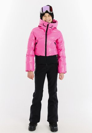Rosa Pufferjacke mit tailliertem Design, hohem Kragen und schwarzen Akzenten, kombiniert mit schwarzen Skihosen und schwarzen Stiefeln. Schneebrille auf dem Kopf.