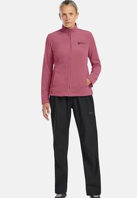 Fleecejacke in Hellrosa mit hohem Kragen und Frontreißverschluss. Kombiniert mit schwarzen Hosen, die einen elastischen Bund und ein Logodetail aufweisen.