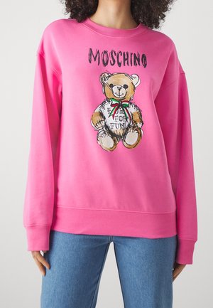 Sweat-shirt rose vif avec un motif d'ours en peluche portant un nœud et le texte « Moschino » au-dessus et « Made for fun » sur le t-shirt de l'ours.