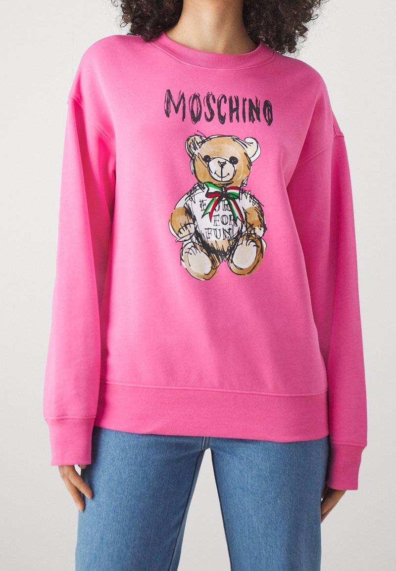 Sweat-shirt rose vif avec un motif d'ours en peluche portant un nœud et le texte « Moschino » au-dessus et « Made for fun » sur le t-shirt de l'ours.