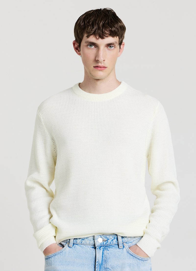 Maglione lavorato a maglia color crema con motivo testurizzato e scollo rotondo, abbinato a jeans in denim azzurro chiaro. Maniche lunghe, vestibilità comoda.