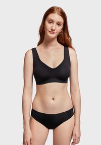 Soutien-gorge sans fil noir avec larges bretelles et un design en v. Texture lisse et finition sans couture. Bas de bikini noir assorti avec des bords festonnés.