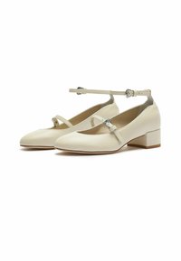 Zapatos de cuero crema con tira en el tobillo, punta redonda y tacón bajo en bloque. Cuentan con una pequeña hebilla decorativa en la tira.