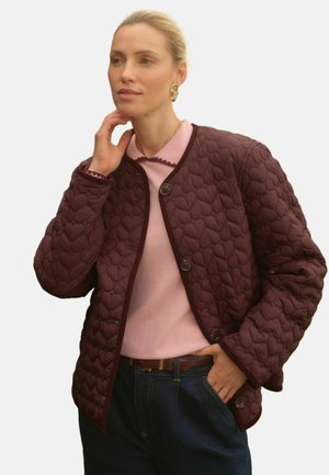 Burgunderfarbene gesteppte Jacke mit herzförmigen Mustern, rundem Ausschnitt und Knopfverschluss. Getragen über einem hellrosa Oberteil und dunkelblauen Jeans.