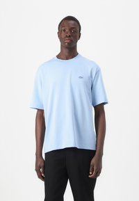 T-shirt bleu clair à manches courtes en matériau doux, avec un col rond et un petit logo brodé sur la poitrine gauche.
