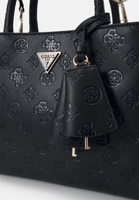 Borsa a mano nera in materiale sintetico con loghi in rilievo, una placca triangolare con logo e una nappina laterale rimovibile con dettagli in metallo dorato.