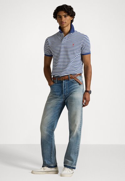 Pasiasta koszulka polo w kolorze niebieskim i białym, połączona z jasnoniebieskimi dżinsami. Ma kołnierzyk, krótkie rękawy i pleciony brązowy pasek. Białe trampki.