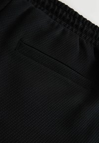 Tissu noir texturé avec ceinture élastique et poche fendue horizontale à l'arrière d'un vêtement.