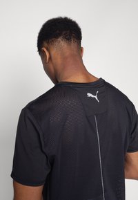 Czarna koszulka sportowa z siateczkowym tyłem, okrągłym dekoltem i logo Puma na szyi. Teksturowana tkanina i dopasowany krój.