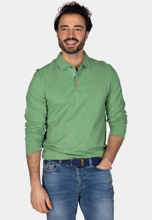 Groene langemouwige polo met een kraag, voorzien van blauwe en oranje knopen, gedragen met blauwe jeans en een geweven riem.
