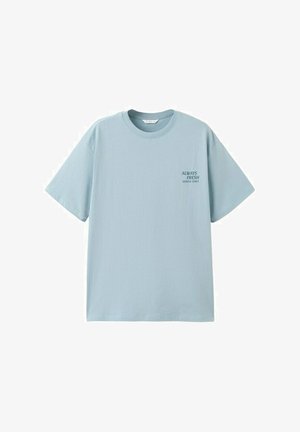T-shirt azzurro chiaro a maniche corte con scollo tondo e piccolo testo "SEMPRE FRESCO SERVITO QUOTIDIANAMENTE" sul petto sinistro.
