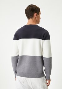 Maglione lavorato a maglia in righe blu navy, bianche e grigie. Presenta un collo rotondo e polsini e orlo a costine. Tessuto morbido con un taglio casual.