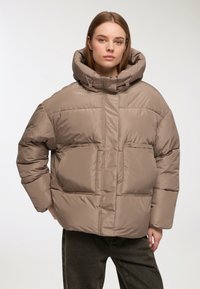 Giubbotto puffo color taupe con cappuccio oversize, due tasche frontali e texture trapuntata. Presenta coulisse per una vestibilità regolabile.