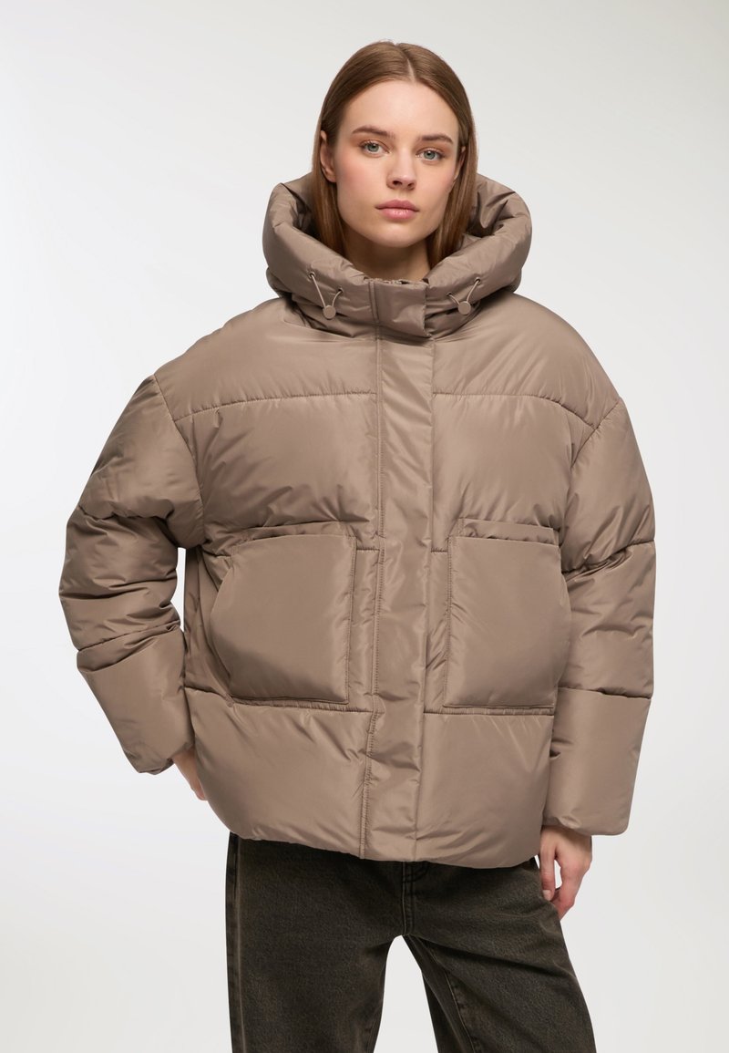 Giubbotto puffo color taupe con cappuccio oversize, due tasche frontali e texture trapuntata. Presenta coulisse per una vestibilità regolabile.