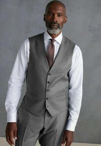 Chaleco de lana gris con solapas y cinco botones, llevado sobre una camisa blanca y una corbata oscura, presenta un corte entallado y una textura suave.