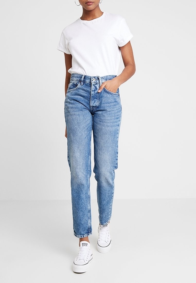 Vit t-shirt med kort ärm som kombineras med högmidjade ljusblå jeans i denim. Jeansen har rak passform, subtila blekningar och framfickor. Vita sneakers.