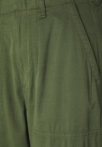 Green cargo shorts made of lightweight fabric featuring a textured pattern and multiple pockets. Stitched accents enhance design detail.