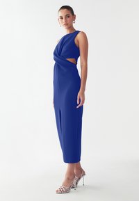 Royal blue jumpsuit with a twisted front design and cut-out detail, made from a textured fabric, paired with silver strappy high-heeled sandals.