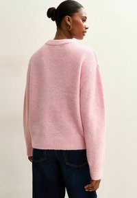 Różowy sweter z dzianiny z kołnierzem, charakteryzujący się miękką teksturą, oversize'owym krojem i ściągaczem na dole, w połączeniu z ciemnoniebieskimi dżinsami.