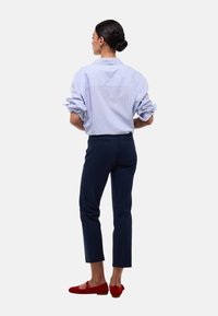 Chemise rayée bleue et blanche avec des manches retroussées, associée à un pantalon slim navy et des ballerines rouges. Pas de motifs ou d'accents remarquables.