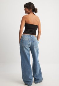 Široke modre kavbojke z blagim obrabljenim videzom, z zadnjimi žepi in rjavim usnjenim žepkom na pasu.