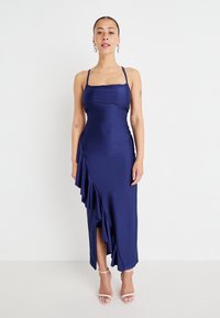 Navy blue satin dress with thin straps, a square neckline, and a cascading ruffle detail along the side, extending to mid-calf length.