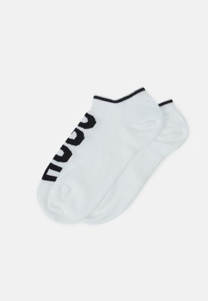 Chaussettes blanches à cheville avec une rayure noire au niveau du bord, logo imprimé en gras noir sur le côté, fabriquées en tissu doux et extensible.