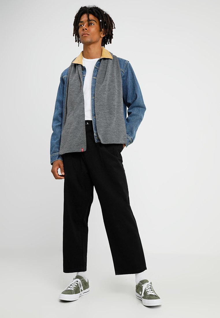 Veste en denim et polaire grise avec col beige, t-shirt blanc en dessous, pantalon large noir et baskets en suède vert.