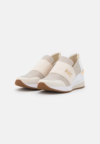 Scarpe slip-on bianche e beige con una tomaia in maglia testurizzata, bande elastiche e suola a zeppa. Presentano un accento del logo dorato.