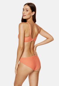 Pomarańczowy zestaw biustonosza i majtek, charakteryzujący się gładką teksturą i regulowanymi ramiączkami. Biustonosz ma zapięcie na haczyk, a majtki mają klasyczny krój.
